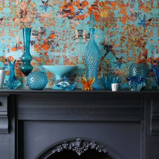 blue glassware sitting on a cast iron mantelpiece in front of feature wallpaper