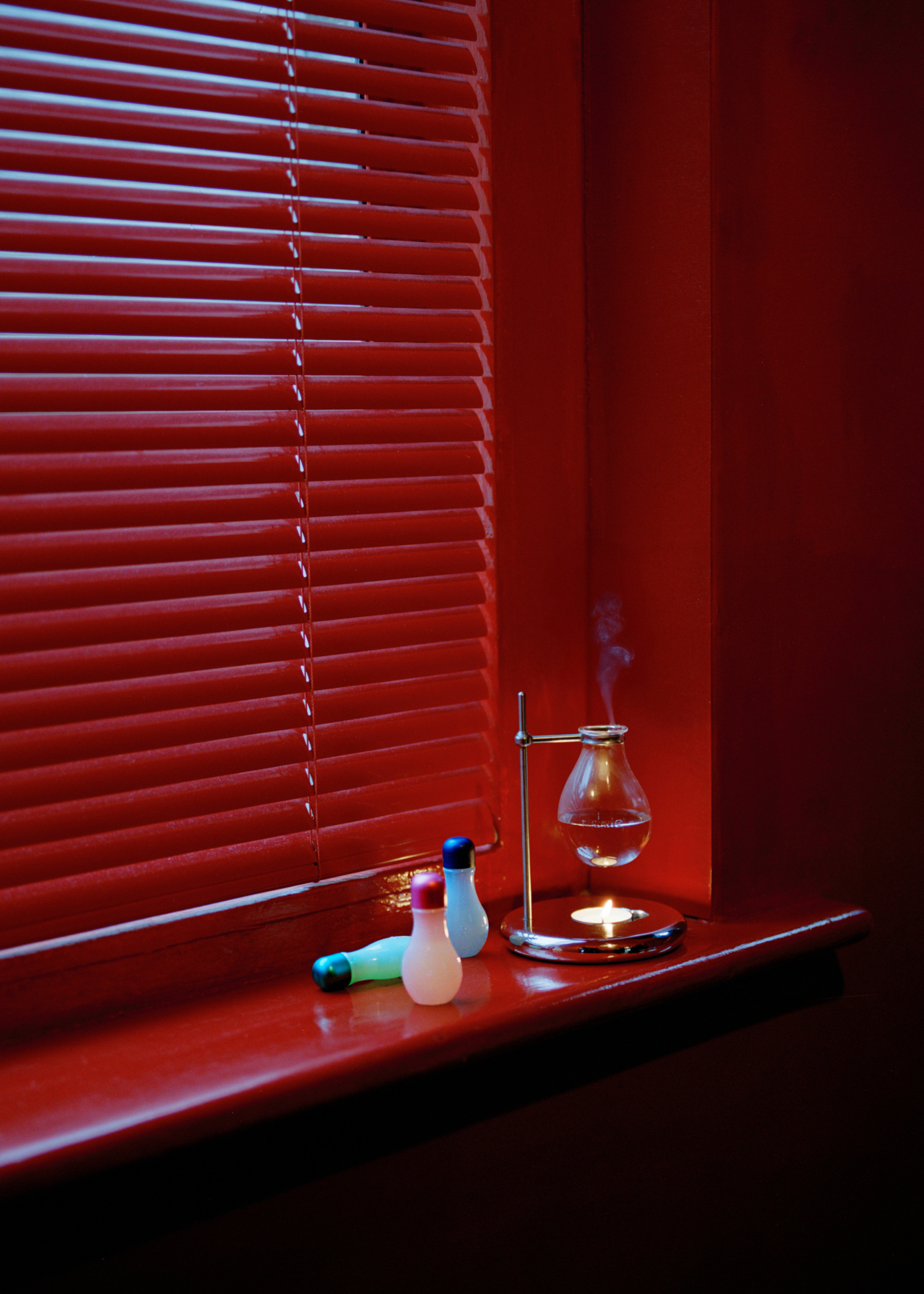 A red window sill with an essential oil burner and colorful oil bottles