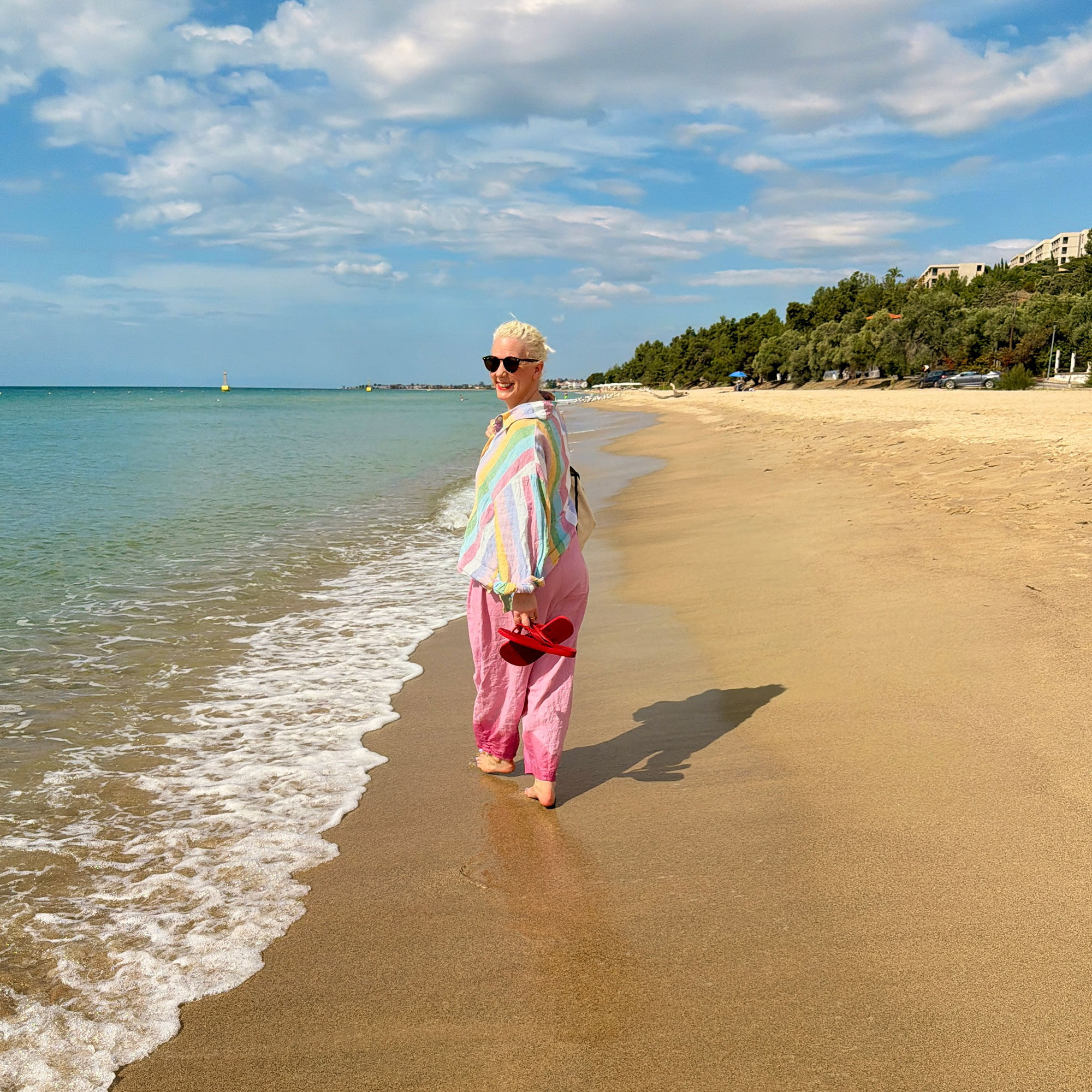 Woman in striped shirt and pink trousers walking along beach