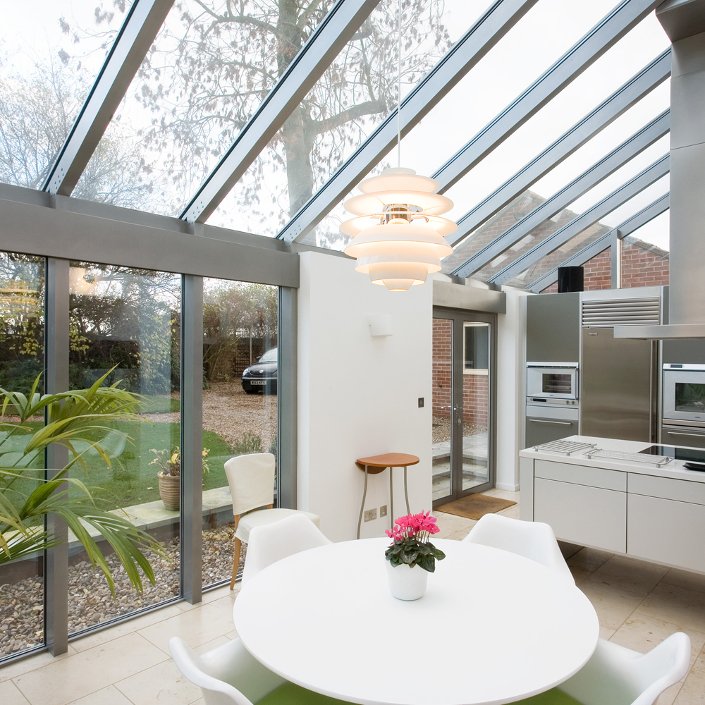 A large conservatory kitchen diner with white kitchen units, dining table and chairs