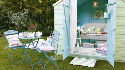 Summer house, painted light green and blue, white wicker sofa inside, floral cushions, small chandelier, blue metal garden furniture outside, checked and striped cushions. Pub origIH 06/2008