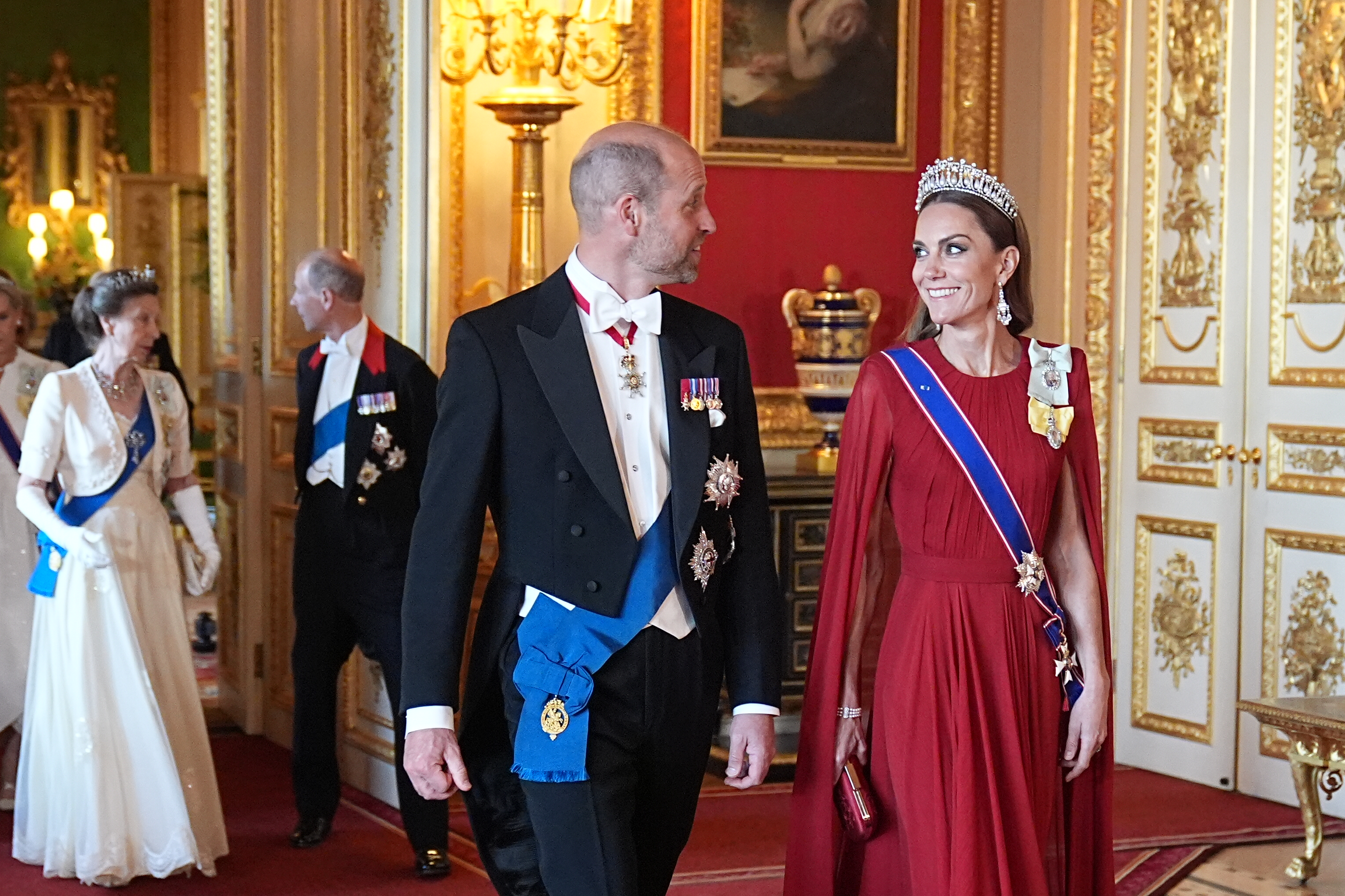 Princess Kate wearing a red gown and tiara smiling at Prince William