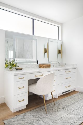 white bathroom with marble topped vanity and make up space. Mirrors, chair for make up vanity end