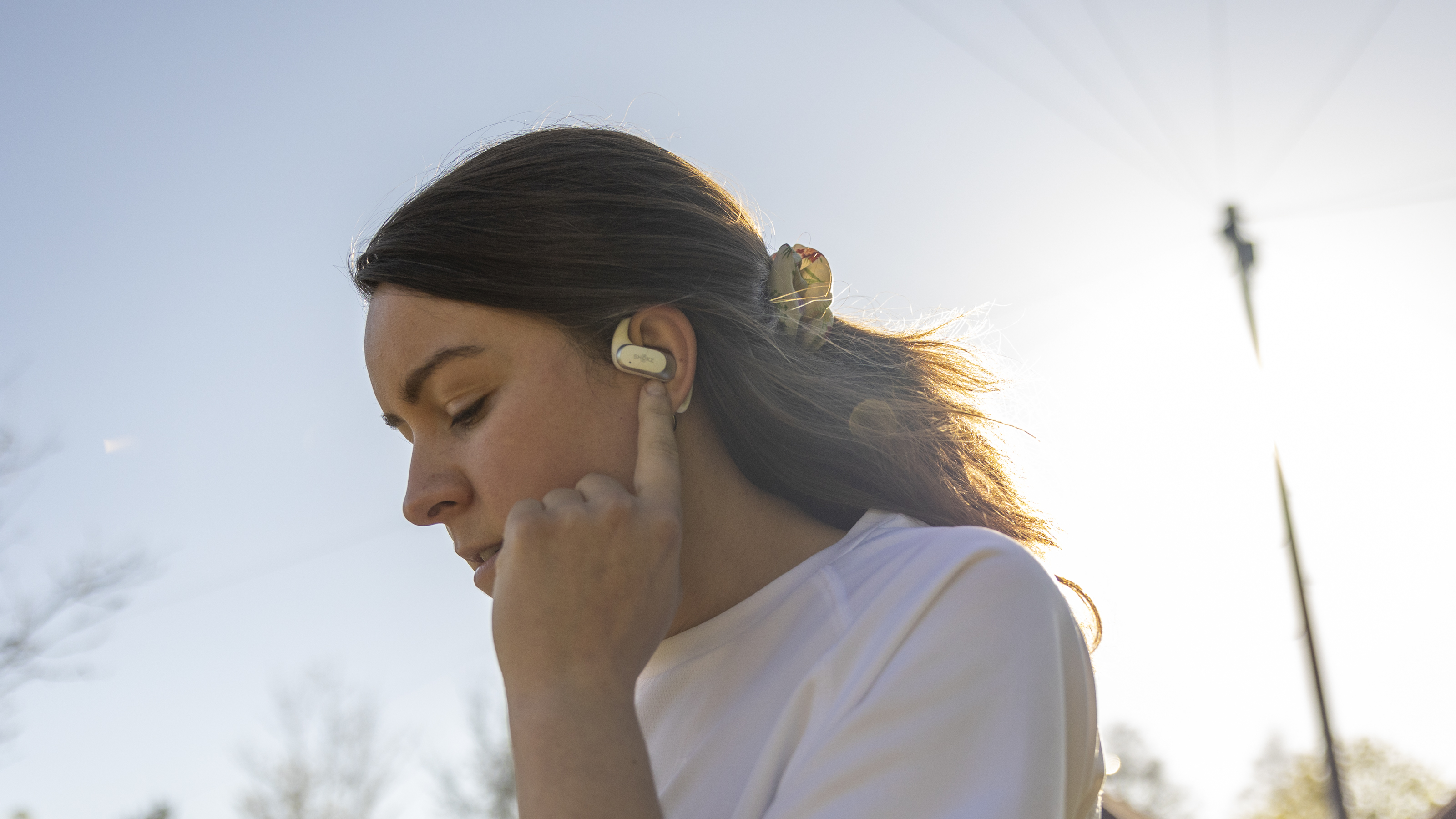 A side view of a female wearing the Shokz OpenFit Air headphones in bright sunshine