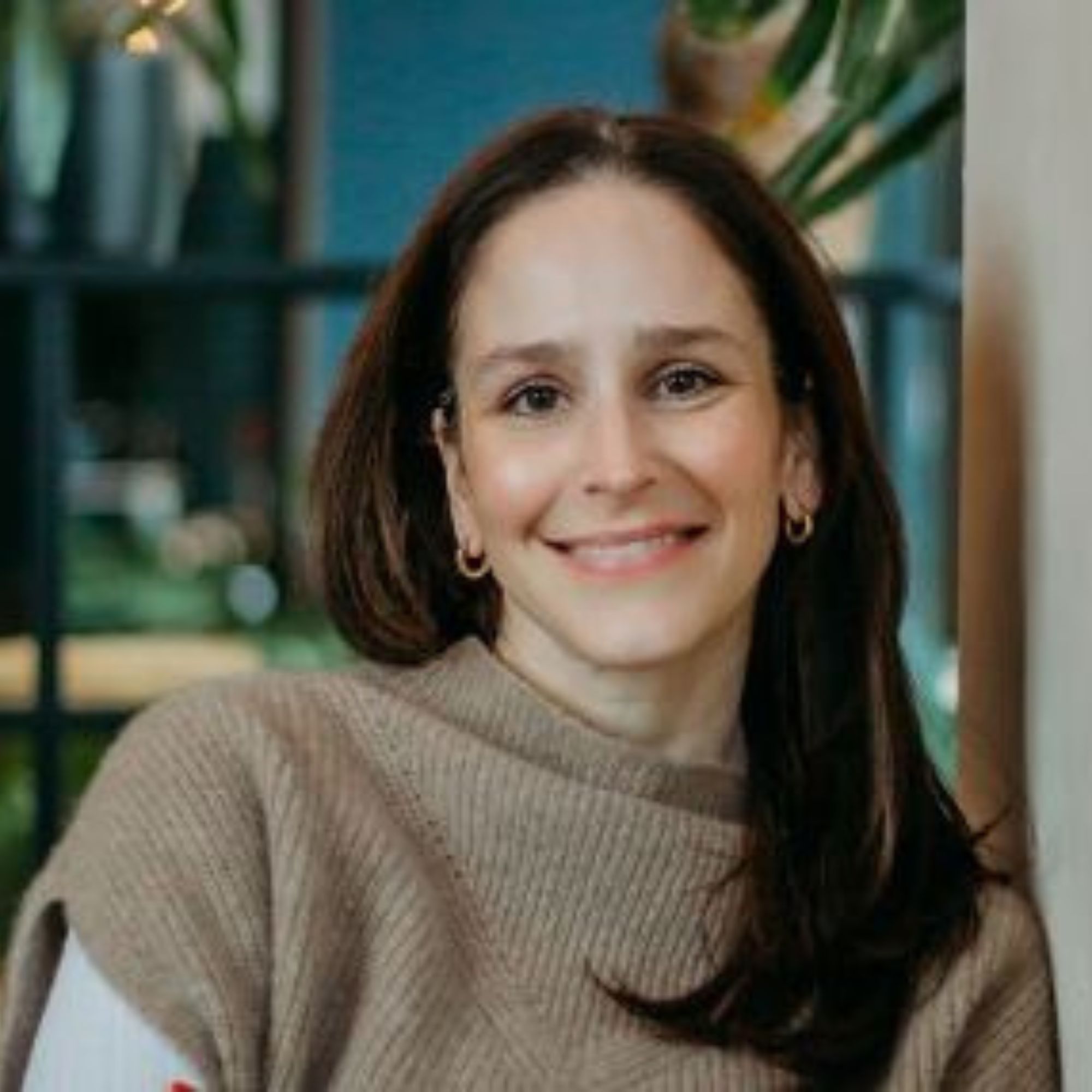 A headshot of Dana Reder - a woman with long brown hair wearing a light brown jumper, smiling into the camera