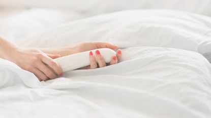 Hand of woman holding sex toy in bed - stock photo
