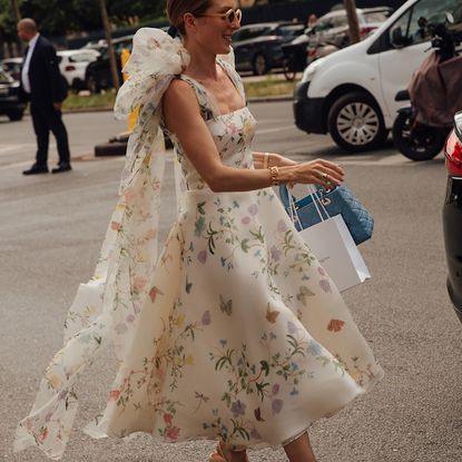 woman wearing a white floral dress carrying shopping bags and a blue handbag