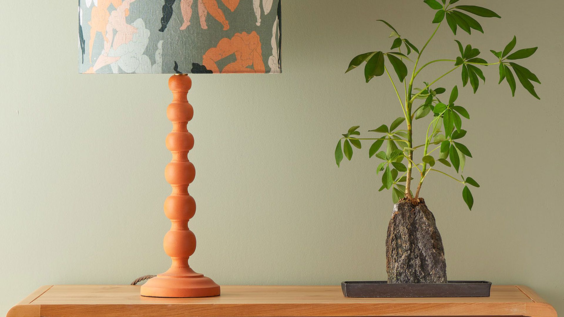 sage green color trend with burnt orange accent lmap base and wooden sideboard with Japanese plant