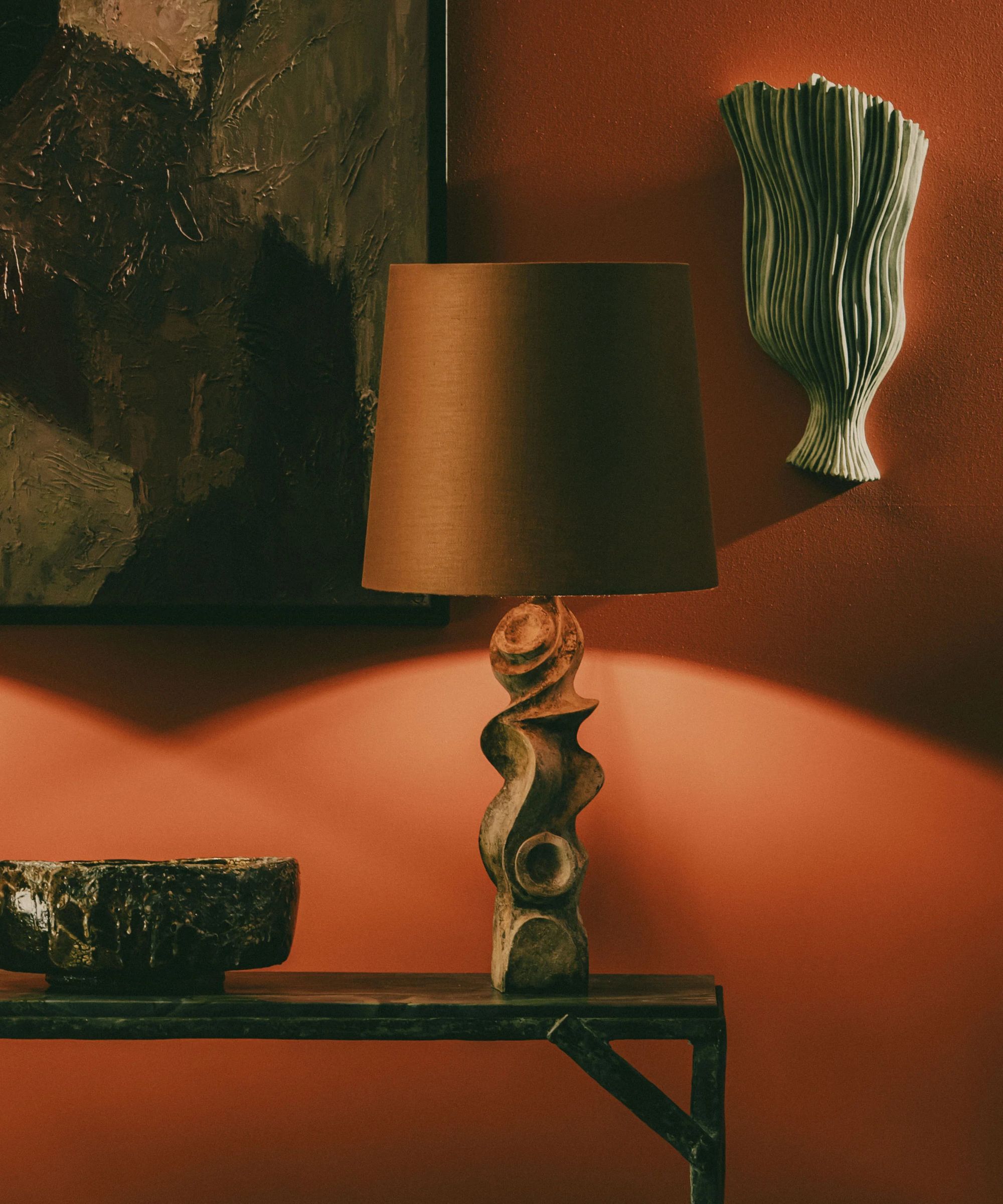 Sculptural lamp with brown shade, red-painted wall in background, artwork and sculptures on wall