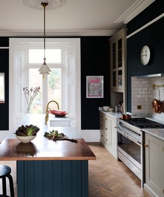 kitchen island color ideas, dark blue kitchen with dark blue painted island with copper countertop one end, white the other, stone cabinetry, herringbone flooring, pendant lights, artwork
