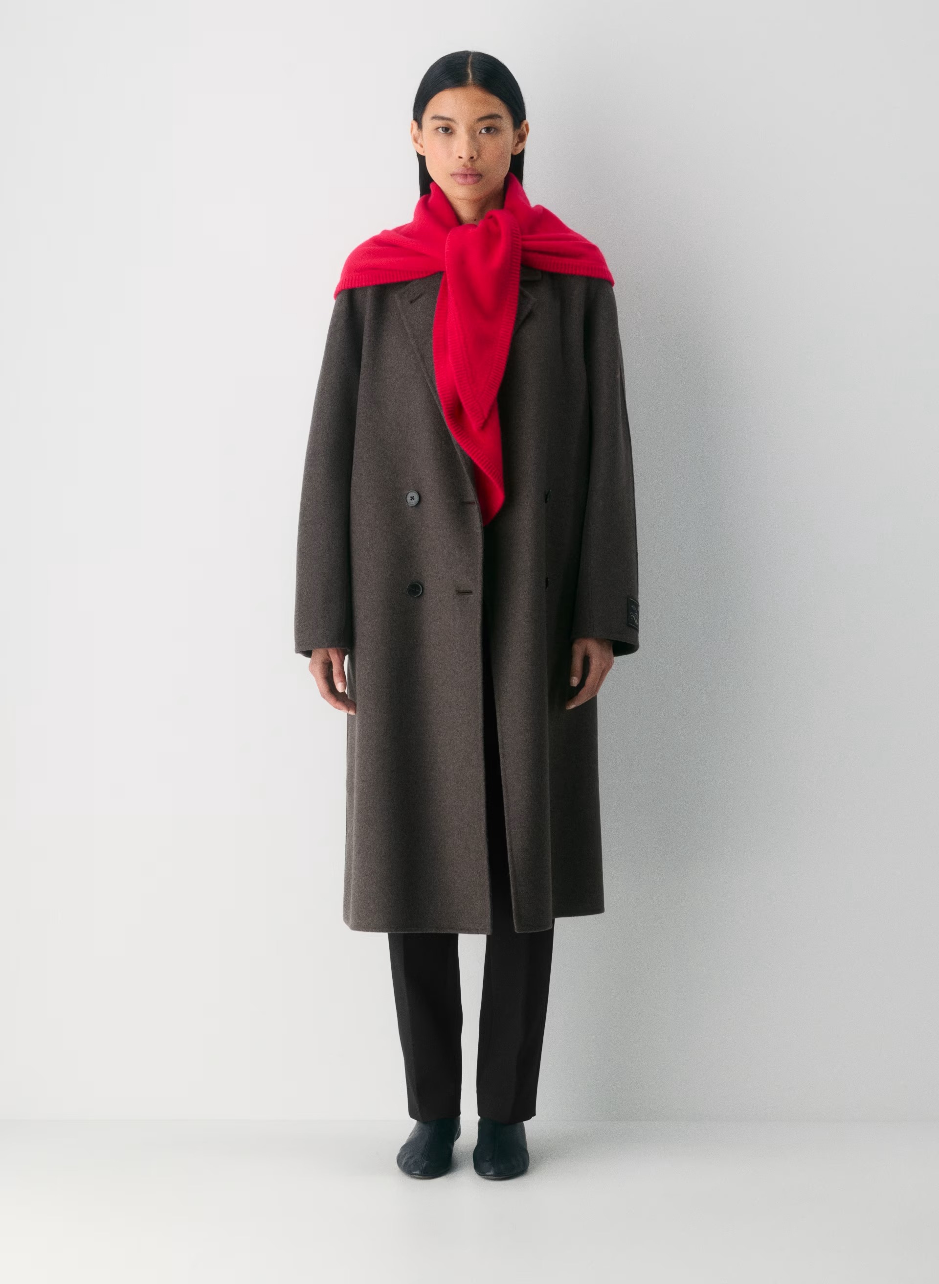 model wears wool double breasted coat, black trousers, black boots, and red triangle scarf 