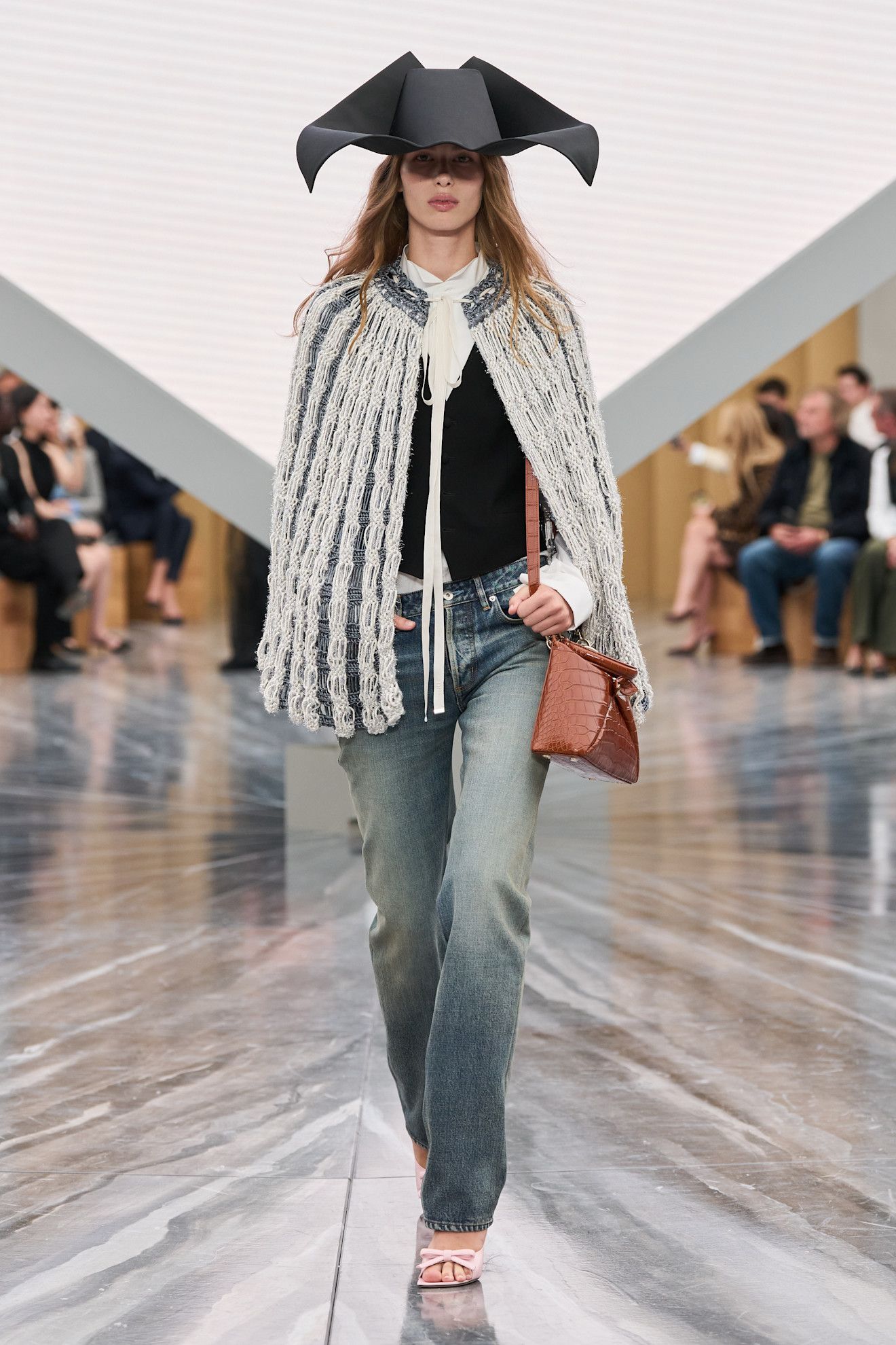 On the S/S 26 Dior runway a model wears washed out jeans, cape and a large hat.