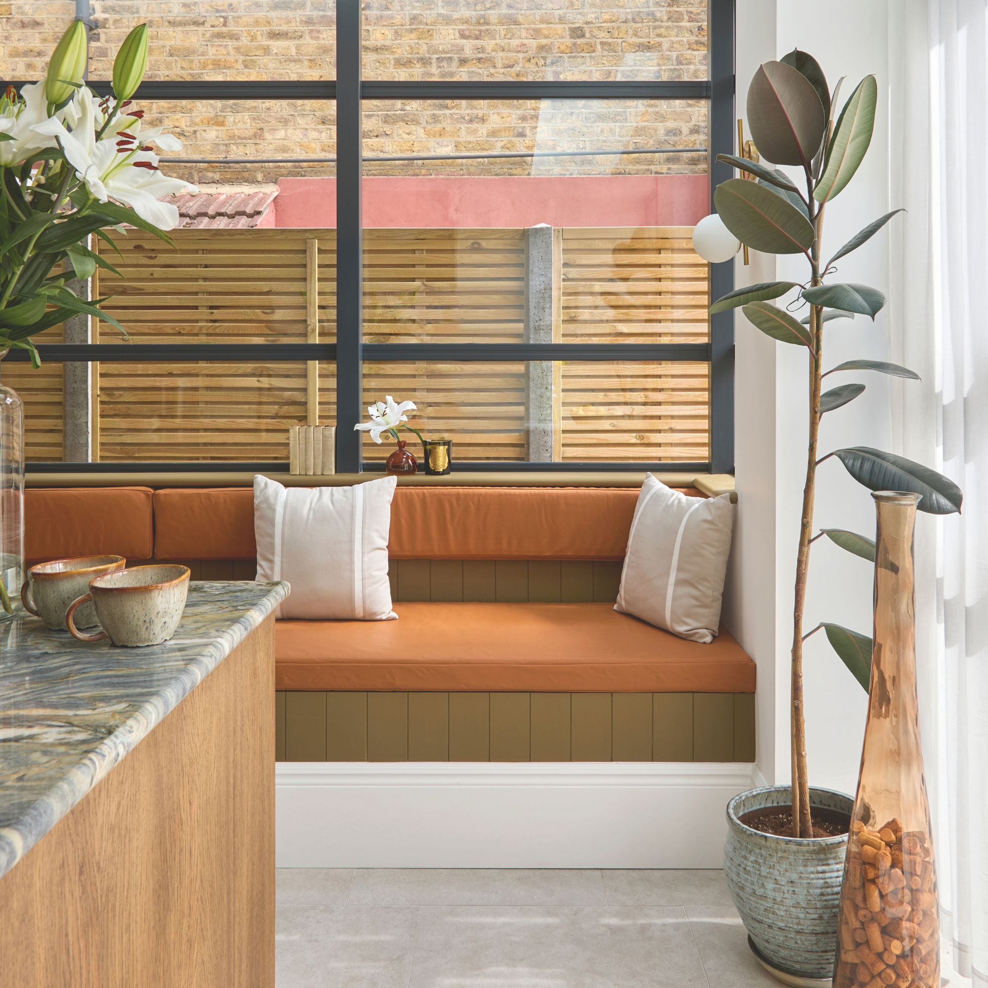Banquette seating with orange cushions and large windows behind it in a kitchen