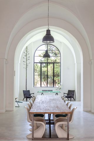 White dining room with a long, wooden dining table and cream chairs. Large window at the far end, looking out into the garden