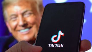 TikTok app on a smartphone with Donald Trump in the background.