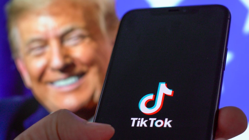 Aplicativo TikTok em um smartphone com Donald Trump em segundo plano.