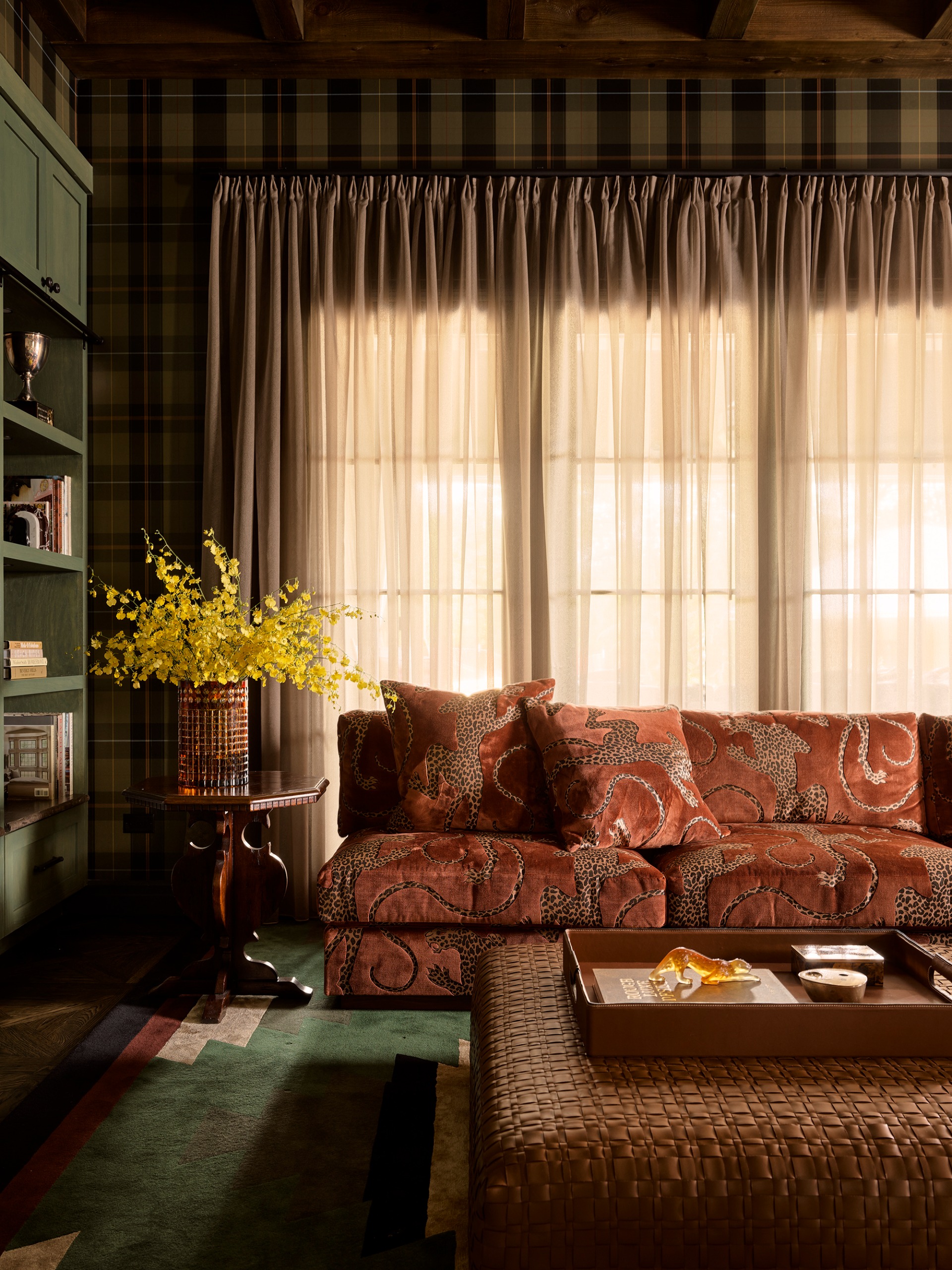 an autumn toned living room with tartan wallpaper, a velvet patterned sofa and green rug