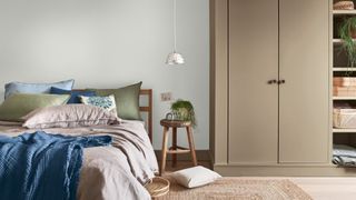 Calming bedroom color scheme in off-white with green linen sheets and brown painted wardrobe beside bed