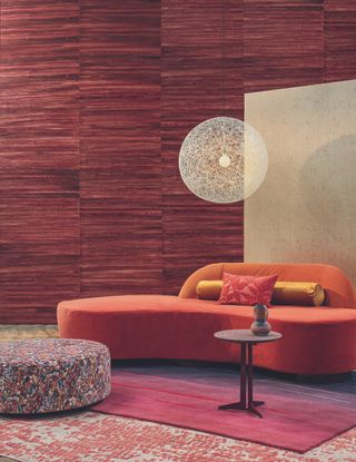 Curved red sofa and patterned ottoman with a spherical light above