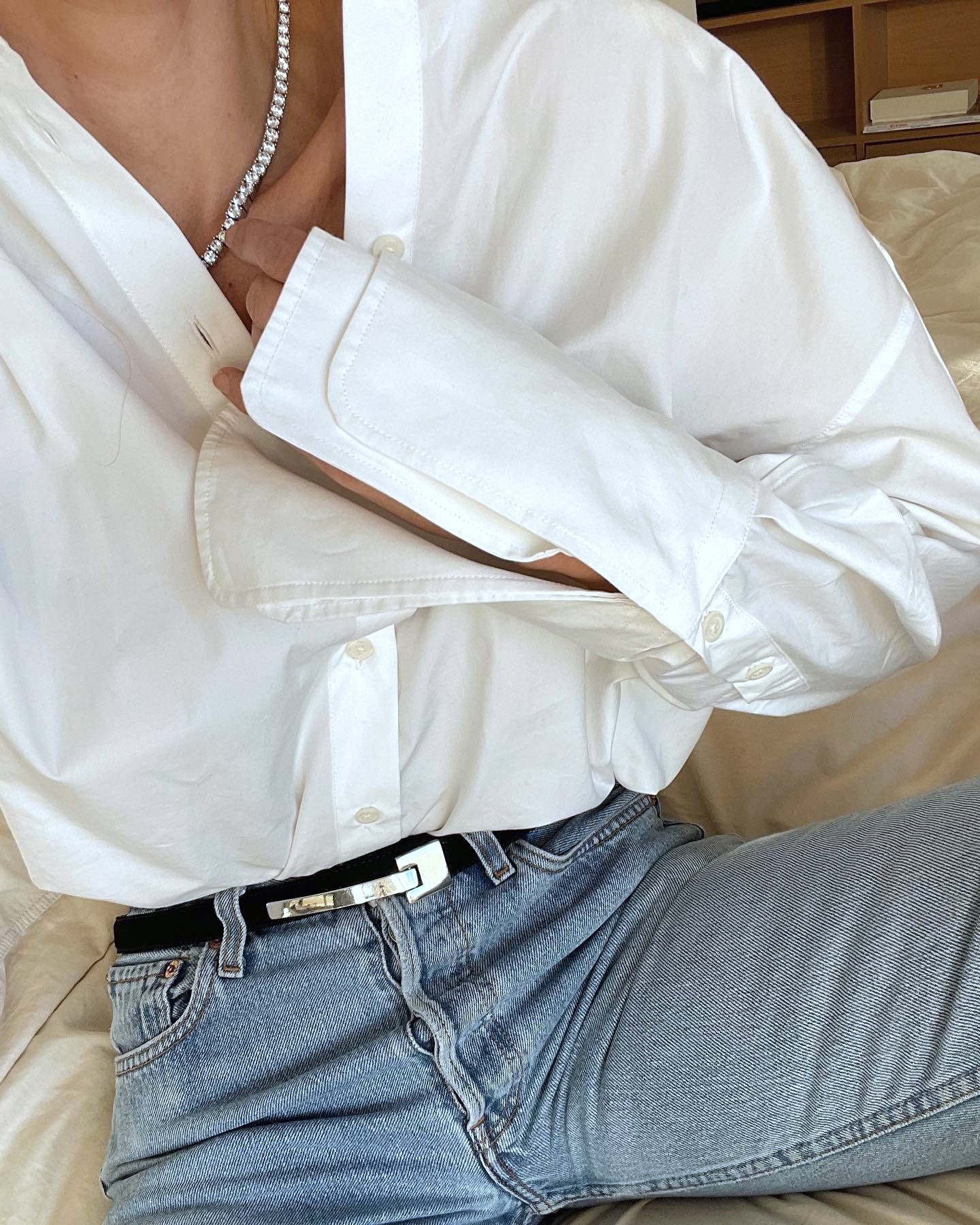close up of style influencer Anouk Yve sitting wearing a diamond tennis necklace, white button-down shirt with oversized cuffs, a black belt with silver buckle, and button-fly jeans