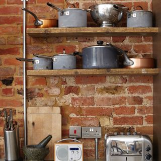 Kitchen brick wall with open shelving displaying shelves of saucepans