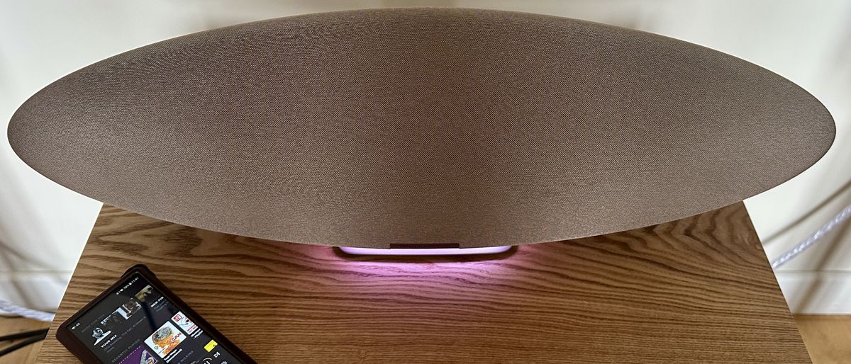 The Bowers &amp; Wilkins Zeppelin Pro Edition on a shelf with a pink light on and a music player laid next to it.