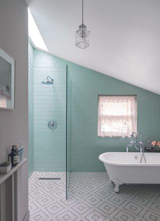 Bathroom with geometric tiled floor, green painted brick wall, roll top bath and walk in shower,