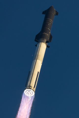 a large black and silver rocket launches into a clear morning sky