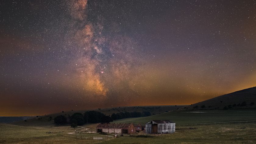 A serene rural landscape at night with an old barn on grassy fields under a starry sky. The Milky Way glows brightly, enhancing the tranquil mood