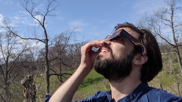 A handsome young man looks up at the sun through solar eclipse glasses on April 8, 2024