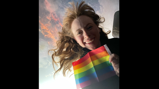 haley arceneaux holding a pride flag in front of a window, with earth in behind