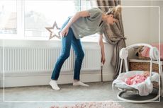 Mother adjusting temperature of radiator while baby sleeps in carrycot on the floor