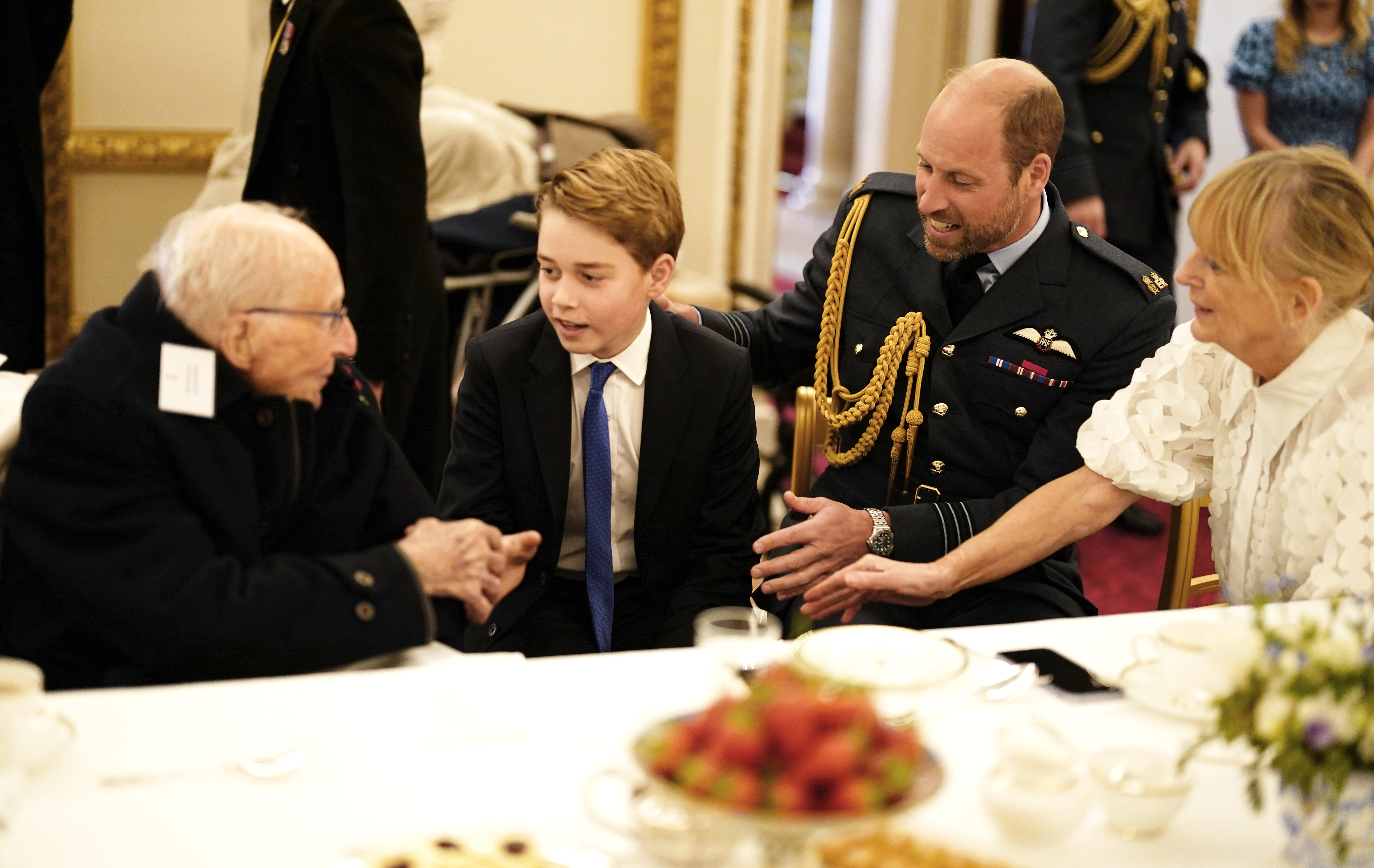 Prince George and Prince William talking to an elderly man at a VE Day tea party