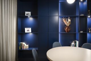 A dining room with navy blue walls, and mid-tone gray chairs