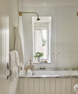 A cream shiplap-clad bath with marble top and white subway tiled wall