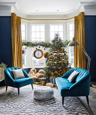 Christmas window decor ideas in a blue living room, with yellow and blue decorations on a foliage garland, matching the Christmas tree decor