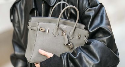 a person holding an hermes birkin bag with a leather jacket in street style