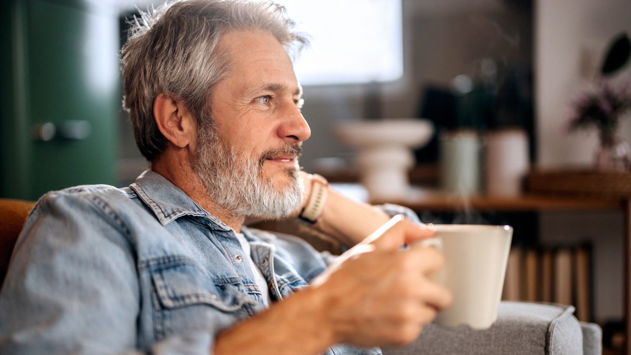 Senior man relaxing on a sofa while drinking coffee at home, calm lifestyle, leisure time and comfortable living concept.