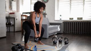 Woman holding a squat with a kettlebell at home following a home workout