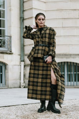 A Paris Fashion Week guest wearing a yellow and black tartan top and skirt with black riding boots