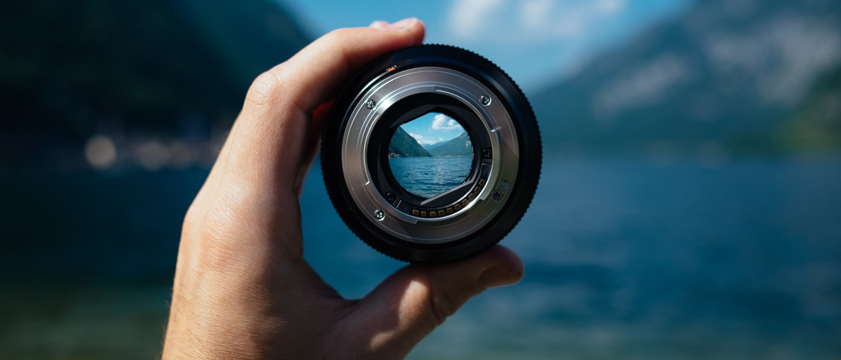 Photographer holding up a lens to view a river and mountain landscape