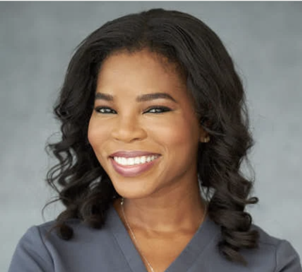 a black woman with dark curly hair wearing a gray top and smiling at the camera
