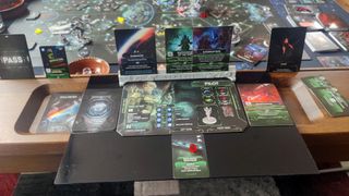 Nemesis character cards, tokens, and more on a wooden table in front of the Nemesis board