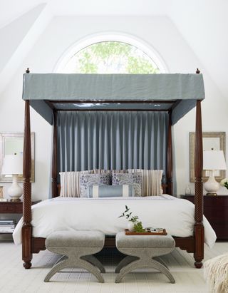 White bedroom with large four poster canopy bed with blue drapes