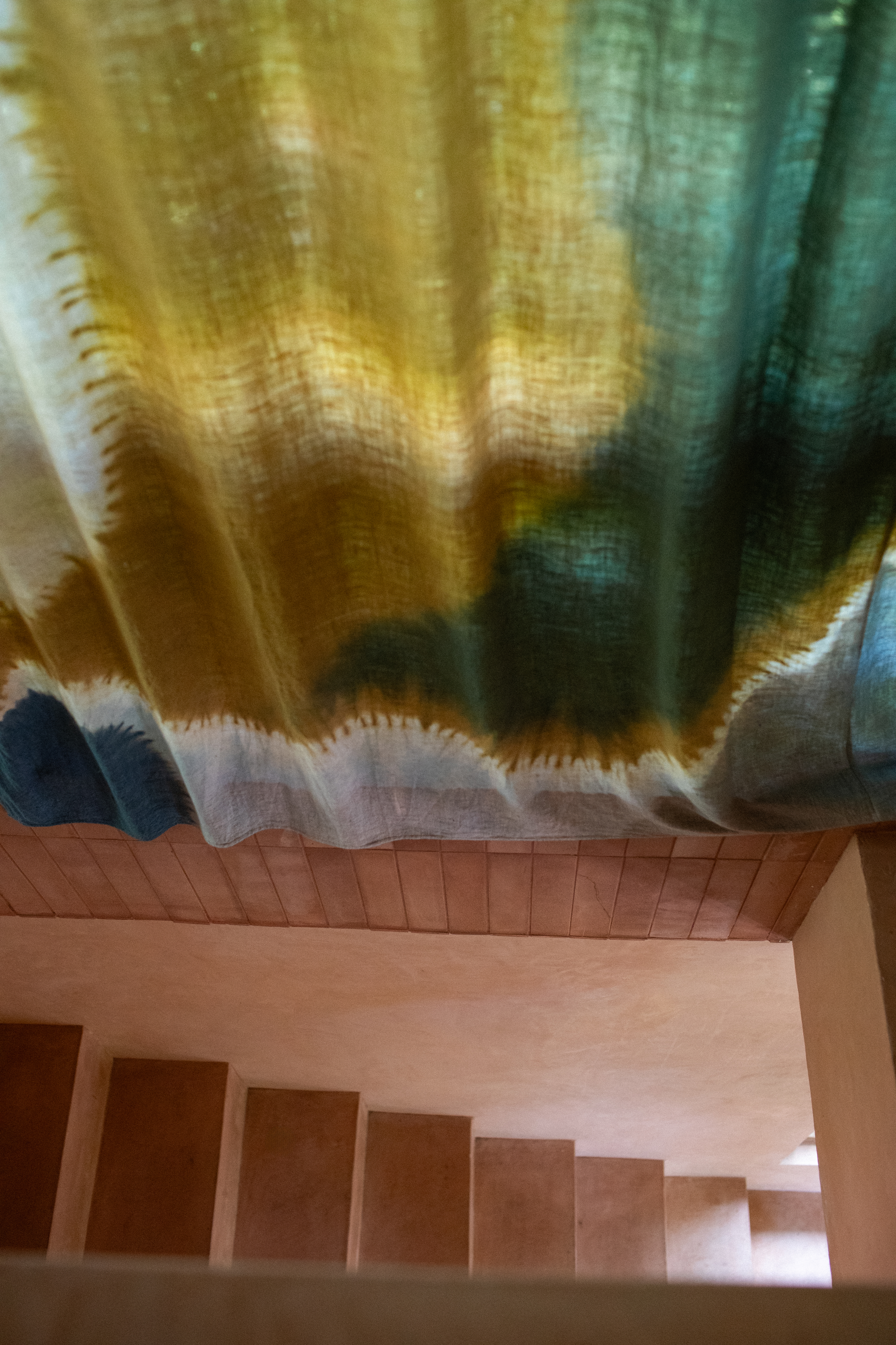 Interiors of a tropical interiors with curved passageways, terracotta walls, colorful curtains, woody furniture, color pops, and nature all around.