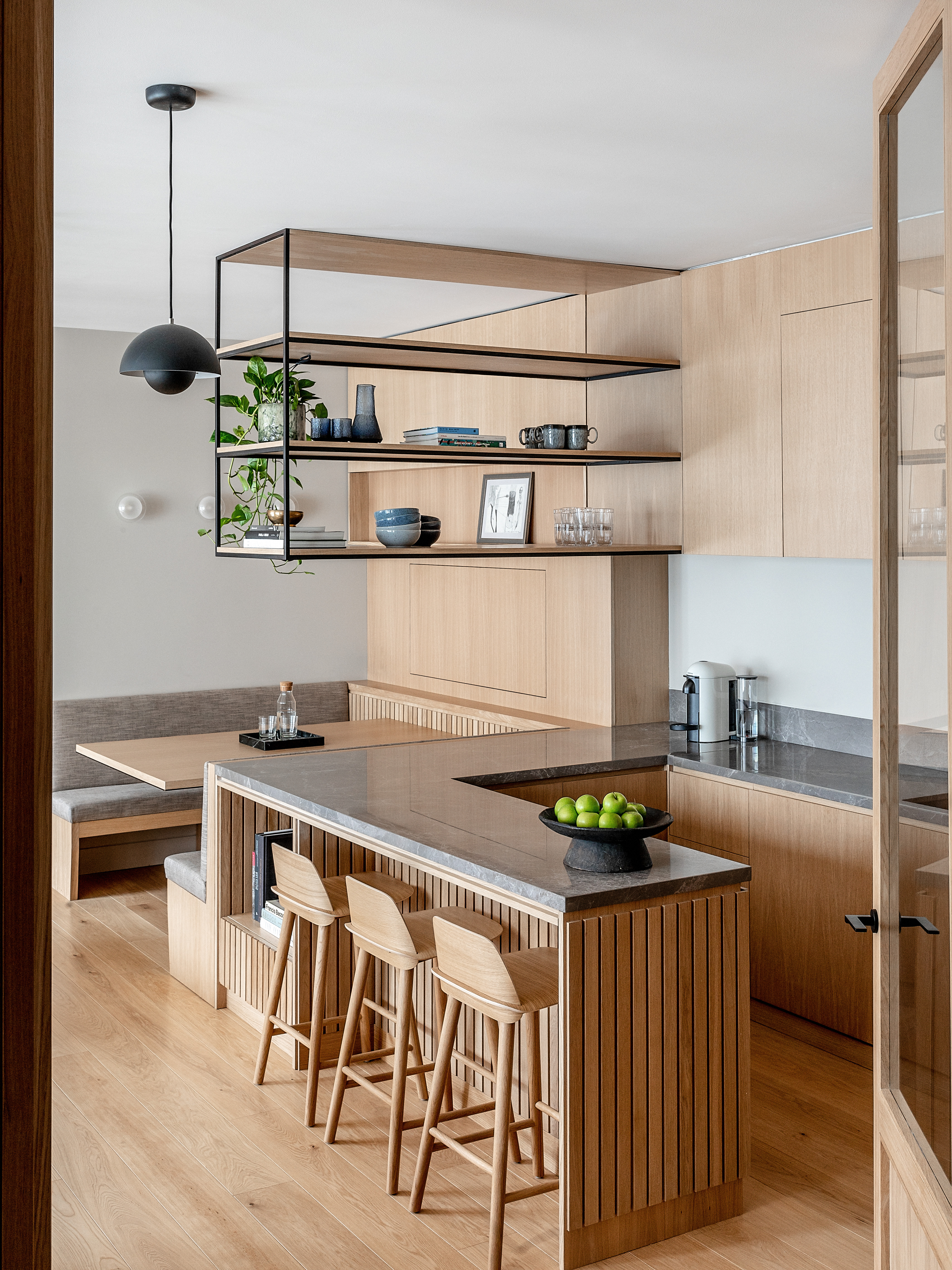 A kitchen island connected to a banquette and bar stool beside it as well as floating open shelving above