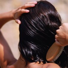 Woman brushing through her wet brunette hair with a wooden brush