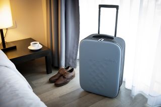 A blue Rollink collapsable suitcase in a hotel room next to a man's brown shoes