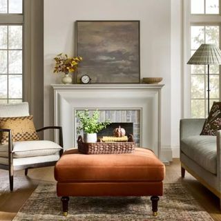 A living room with an orange ottoman and a white fireplace