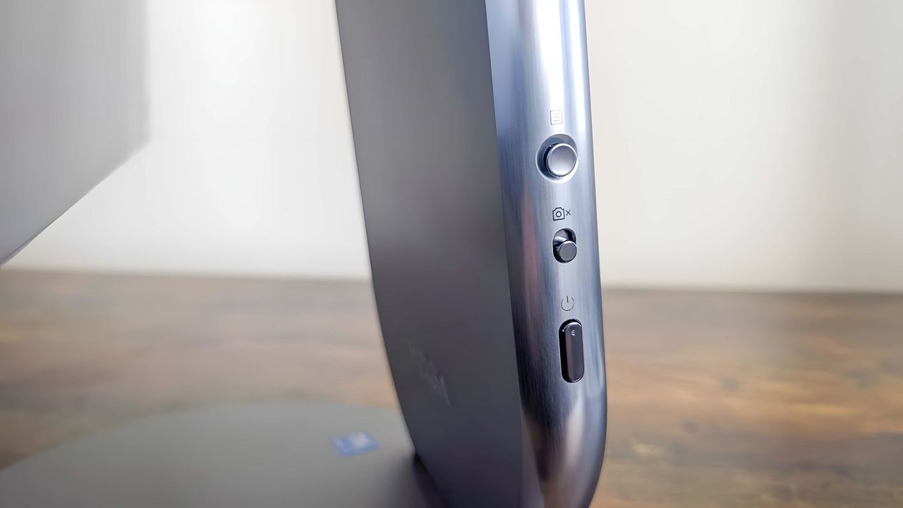 A closeup of the buttons on the left side of the Lenovo Yoga AIO 27"'s stand, which include an OSD joystick, camera switch, and power button.